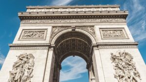 Billede af Triumfbuen i Paris set fra bunden op mod himlen med detaljeret skulpturarbejde på begge søjler og en klar blå himmel i baggrunden