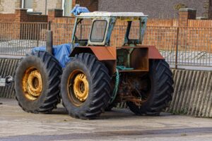Traktor med store dæk parkeret på en cementoverflade med mure og bygninger i baggrunden