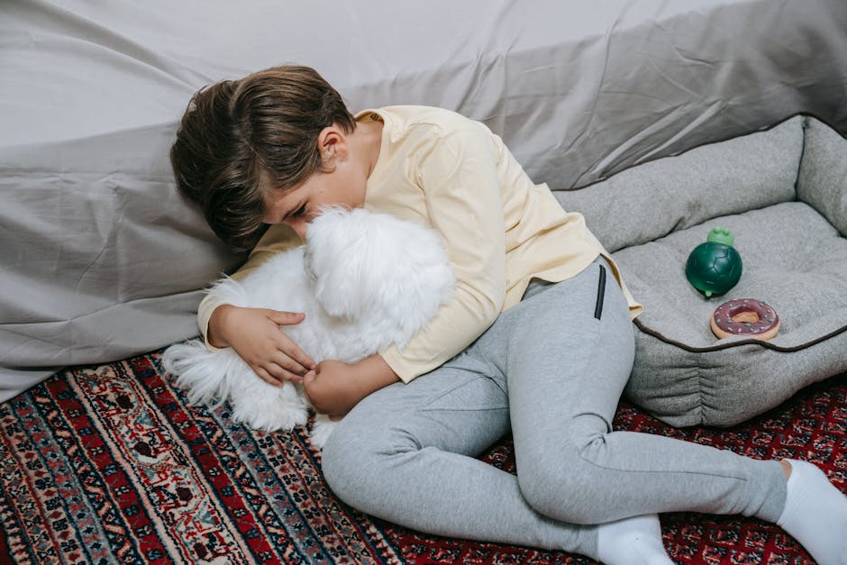 Barn ligger på et tæppe og krammer en lille hvid hund mens der ligger legetøj i nærheden