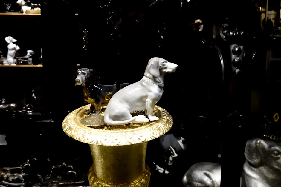 En hvid porcelænsfigur af en hund, der sidder på en udsmykket gylden pedestal med en sort porcelænsfigur af en hund bagved, i en mørk baggrund fyldt med forskellige hundefigurer